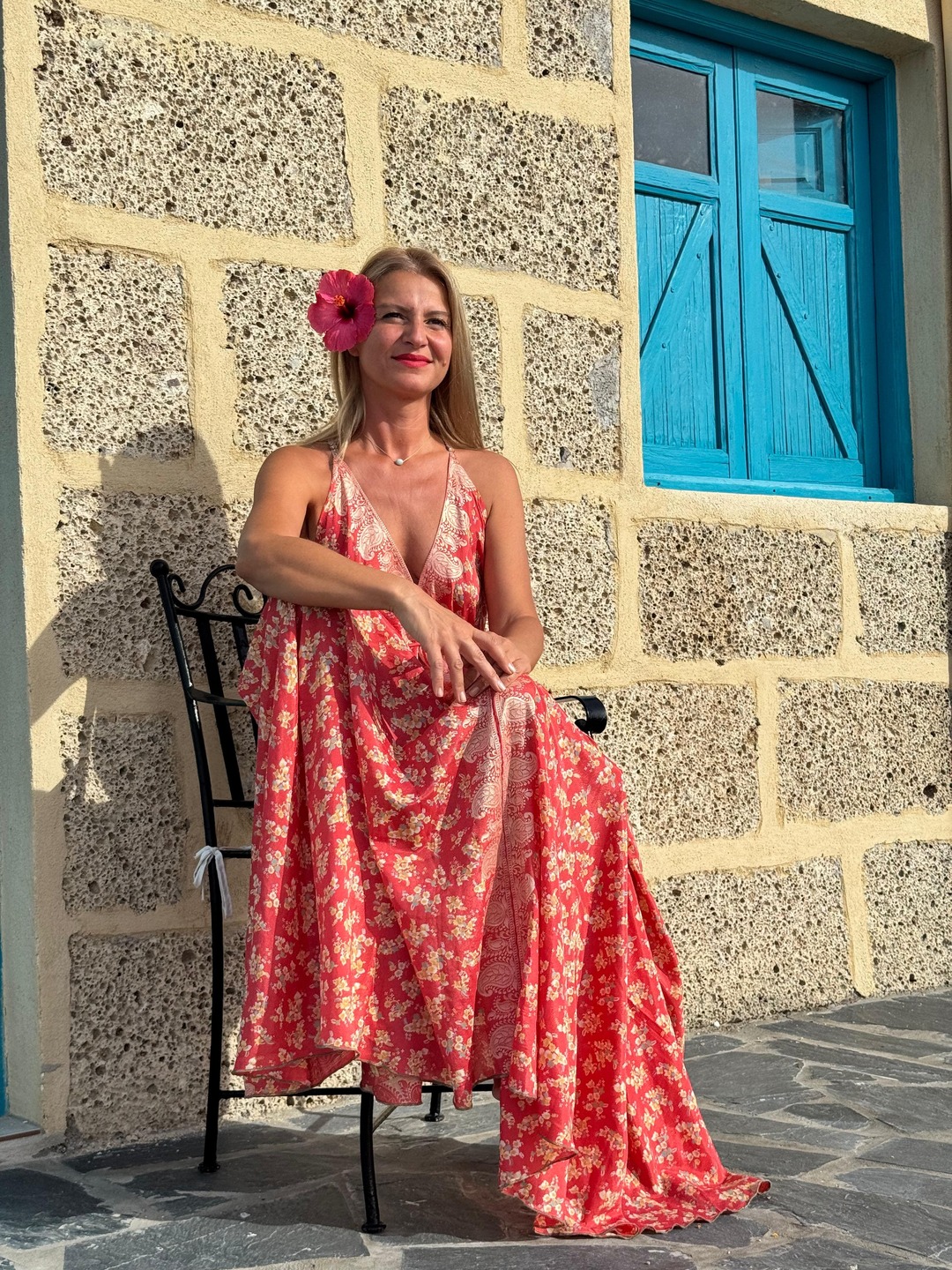 Femeie într-o rochie florală roșie, relaxată lângă un zid de piatră din Tenerife
